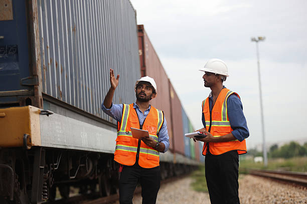 Two Indian logistic staff with safety jacket and PPE check container on rail transportation ,World wide logistic, The container cargo shipment by rail transportation , Logistic manager and staff working check container on rail way