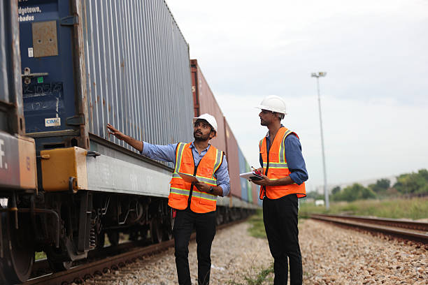 istock Two Indian logistic staff with safety jacket and PPE check container on rail transportation ,World wide logistic, The container cargo shipment by rail transportation , Logistic manager and staff working check container on rail way 2217202051