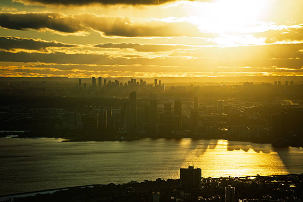 Dramatic sunset over the Toronto skyline with golden light reflecting on the lake and high-rise silhouettes creating a striking contrast under glowing clouds.