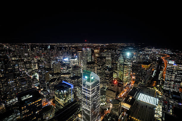 Stunning aerial view of downtown Toronto at night, featuring illuminated skyscrapers, busy streets, and the glowing cityscape extending to the horizon.