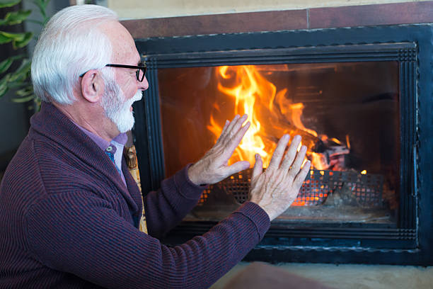 Happy senior man warming up in front of the fireplace at home in winter