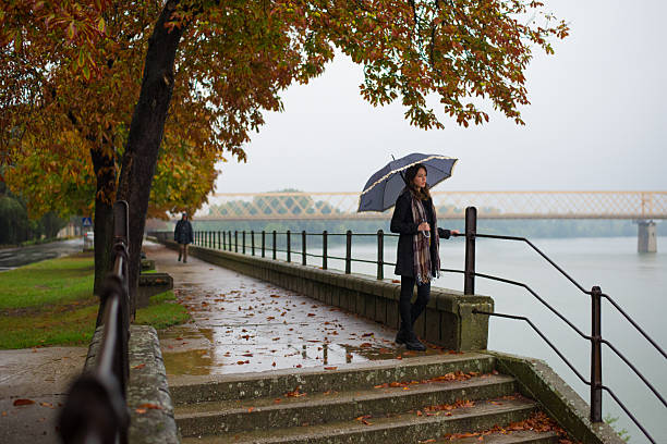 Young brunette woman holding an umbrella walking in the autumn rain.