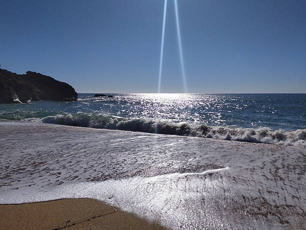 Serene beach scene under bright sun. Waves gently rolling onto shore, creating glistening textures. Ideal for travel, nature, or relaxation themes.