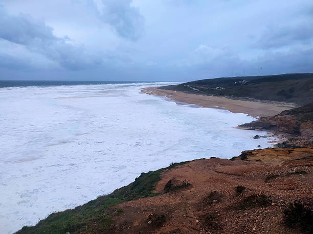 Dramatic seascape featuring powerful waves crashing onto a sandy beach beneath a stormy sky, evoking themes of natures force, coastal beauty, and solitude.