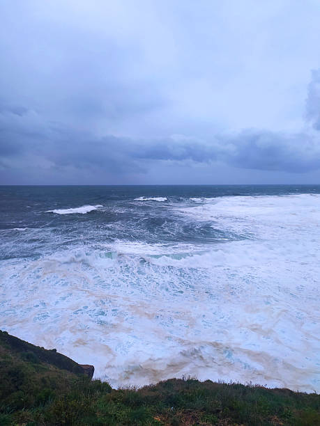 Dramatic seascape featuring powerful waves crashing against a rugged coastline under a stormy, overcast sky. Evokes themes of natures force, resilience, and the sublime.