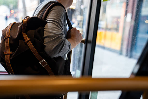 istock A person holding a brown backpack, getting off a bus while gripping the door handle. The image captures the typical commuter moment in an urban setting 2217228799