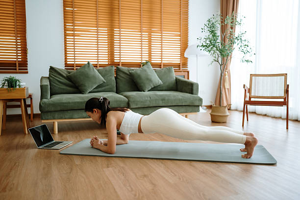 istock Young Asian woman in sportswear doing plank on training mat while watching online workout tutorials on laptop in the living room. Sport and recreation concept 2217242654