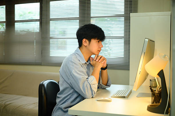 istock Young man working from home, sitting at desk and concentrating on desktop computer screen 2217245505
