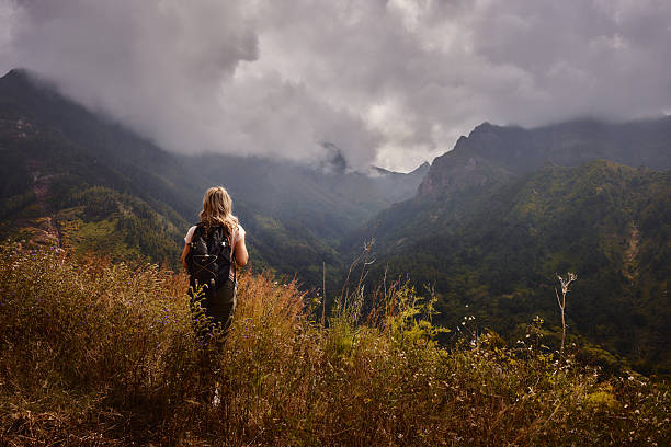Rear view of carefree female backpacker hiking through tall grass on a mountain. Copy space.