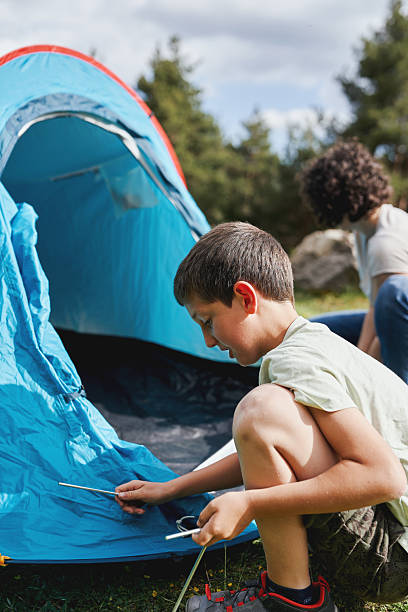 istock Focused boy setting up tent outdoors, learning sustainable camping skills 2217248556