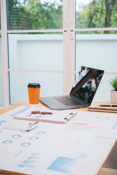 istock A bright, modern office space with a wooden desk covered in documents, charts, a laptop, and a coffee cup. A white chair and large windows create a clean, productive atmosphere. 2217248812