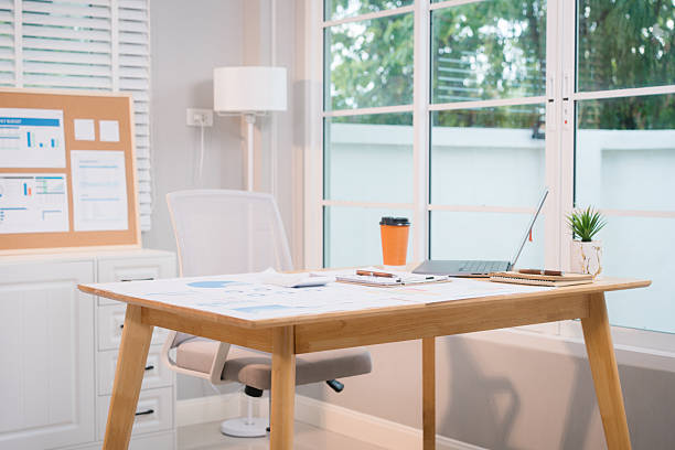 istock A bright, modern office space with a wooden desk covered in documents, charts, a laptop, and a coffee cup. A white chair and large windows create a clean, productive atmosphere. 2217248816