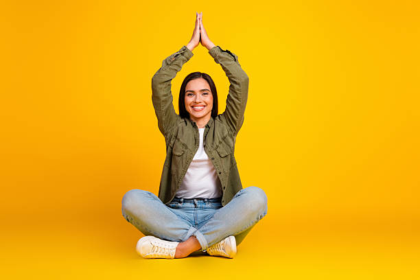 istock Smiling young woman practices meditation gesture while sitting on a colorful yellow background in casual outfit 2217250407