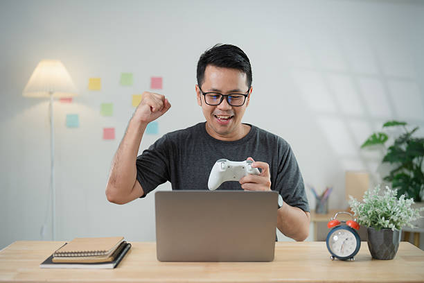 istock Young man celebrating victory while playing video games on laptop in cozy modern workspace with cheerful atmosphere and vibrant decor 2217251469