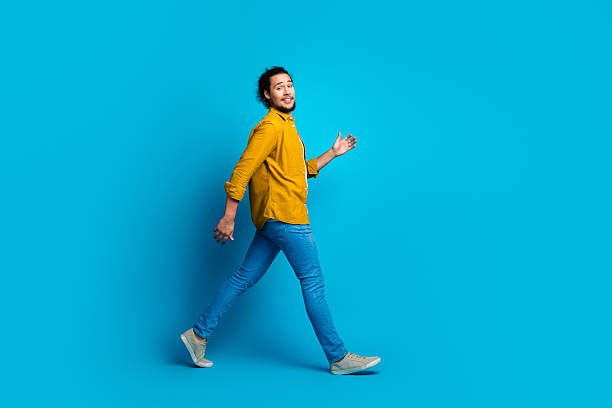 istock Stylish young man walking confidently against a bright blue background, showcasing modern fashion and expressing happiness 2217251517