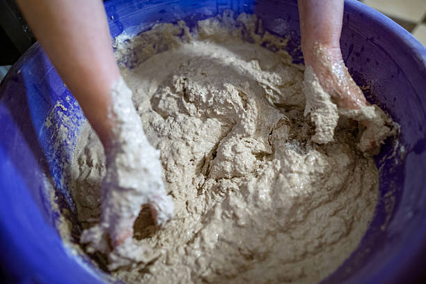 istock Hands kneading dough in a large plastic container during the process of preparing homemade bread. The dough is sticky and textured, showing active mixing. 2217268511
