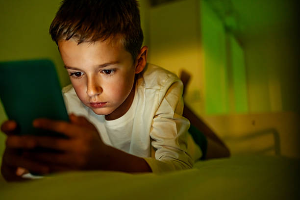 istock Young Boy Focusing on Smartphone Screen in Cozy Evening Lighting 2217270242