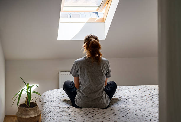 istock Woman sitting crosslegged on bed and looking out window 2217273397