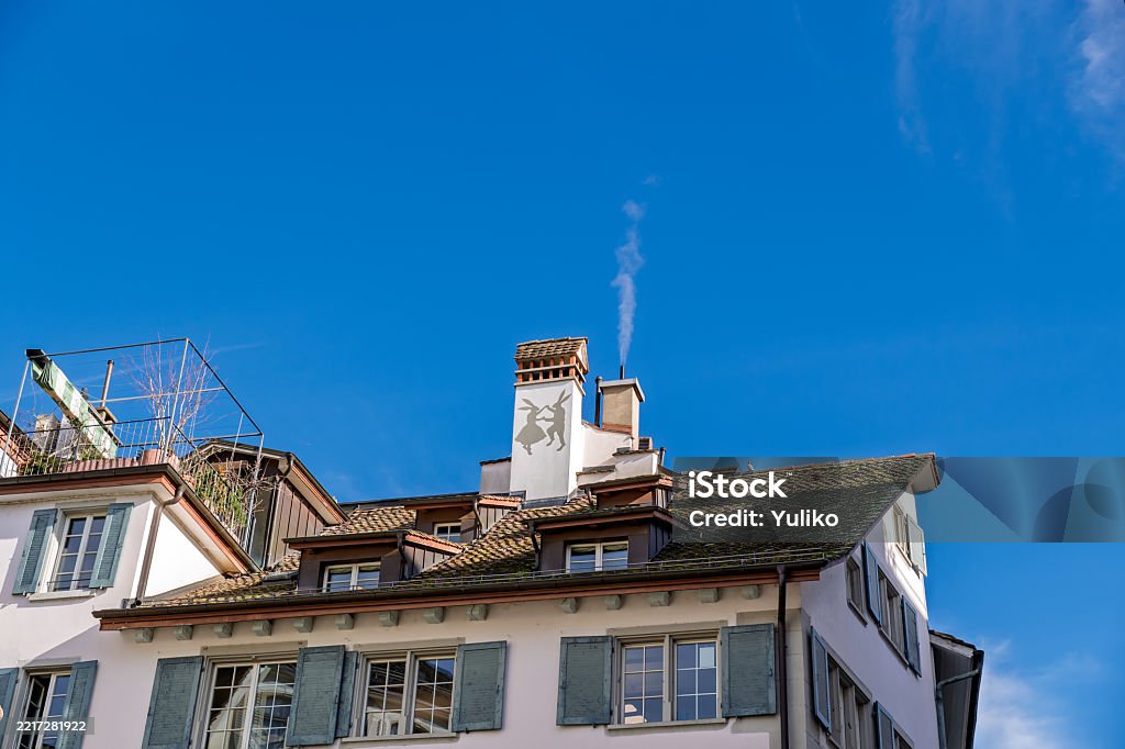 Telhado europeu: chaminé de fumo com silhueta animal contra céu azul claro. - Foto de stock de Aconchegante royalty-free Telhado europeu: chaminé de fumo com silhueta animal contra céu azul claro. - Foto de stock de Aconchegante royalty-free