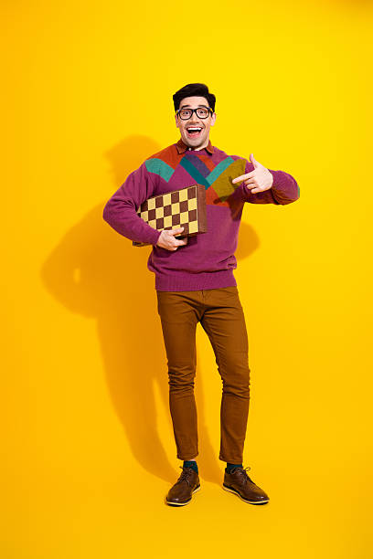 istock Cheerful man holding a chessboard and making a pointing gesture, retro style with colorful sweater against yellow vertical background 2217282402