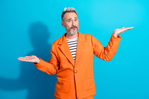 istock Stylish mature man in an orange suit gesturing with both hands against a bright blue backdrop expressing thought 2217284327