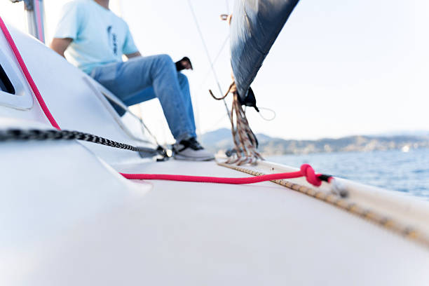 Low angle view of sailboat deck with ropes and blurred sailor sitting on stern enjoying marine journey