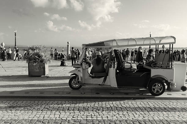 Lisbon, Portugal - November 2, 2024: A tuk-tuk driver waits for clients while sitting in her tuk-tuk at the Praça do Comércio square in Lisbon downtown.