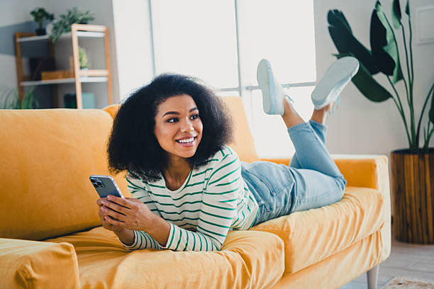 istock Young Woman Using Smartphone on Comfortable Yellow Sofa in Bright Living Room with Modern Decor and Green Plants 2217287182