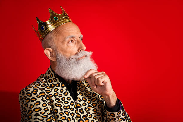 istock Stylish elderly gentleman wearing a crown and leopard print jacket against a red background showing elegance and charisma 2217289942