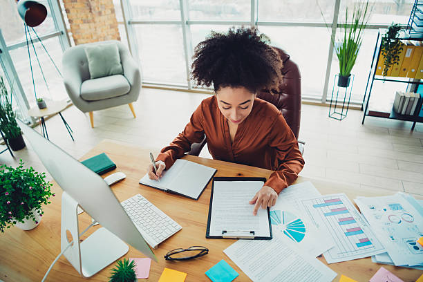 istock Young professional woman working in a modern stylish office space with documents and computer, focused business activities 2217292312