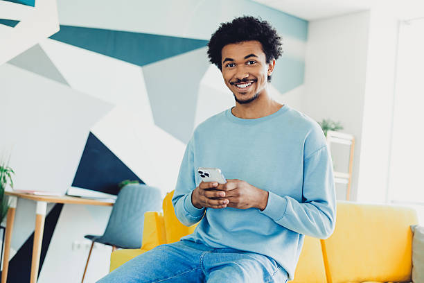 istock Smiling young man with smartphone relaxing in cozy home environment during a bright day 2217292598