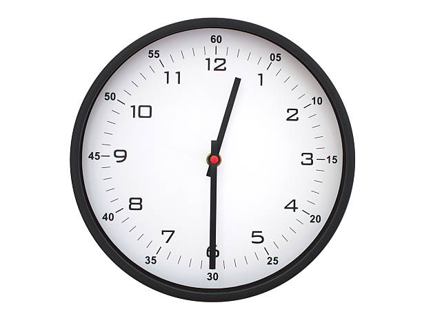 Simple round wall clock with black frame and white face, showing the time exactly at 00:30 or 12:30. Representing time precision in concepts of deadlines.