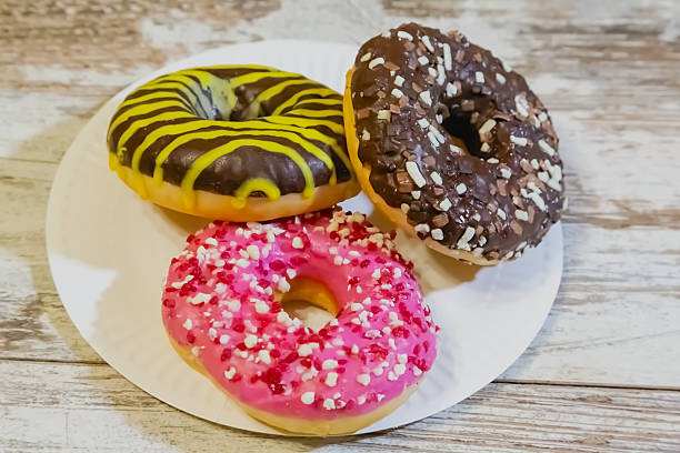 istock Doughnuts with various glazes and sprinkles on a white plate on a wooden table, close-up. 2217295135