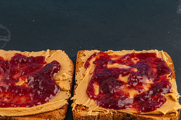 istock Peanut butter and jelly toast preparation on dark surface 2217295940