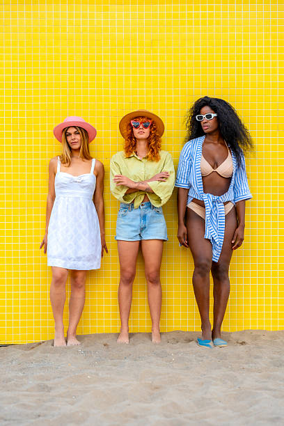 istock Three young women posing on a beach against a vibrant yellow wall 2217306364