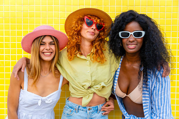 istock Three happy multi-ethnic girlfriends embracing and smiling in front of a yellow wall 2217306369