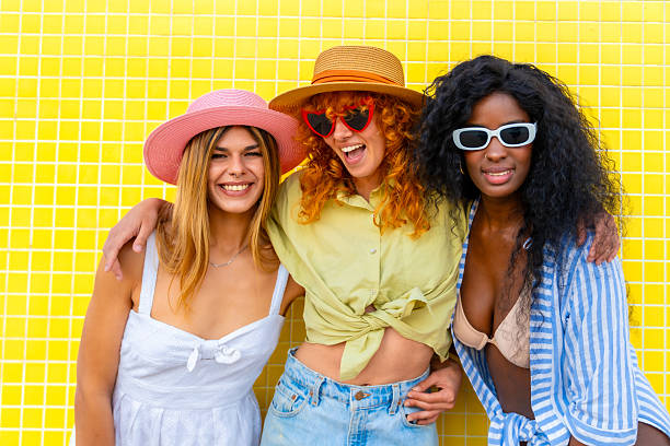 istock Three young women embracing and smiling by a yellow tiled wall 2217306382