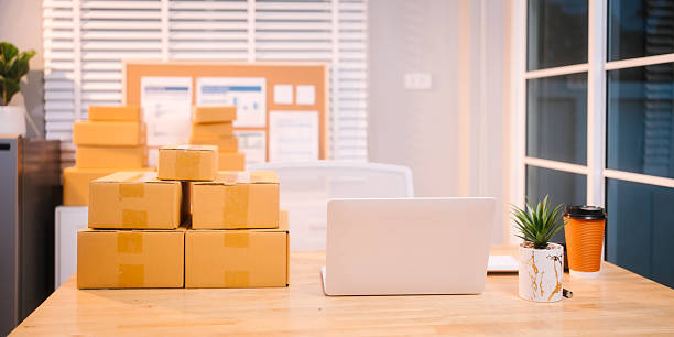 istock A neat workspace with a white laptop, stacked delivery boxes, a coffee cup, and a potted plant on a wooden desk, indicating a busy day of online sales packaging and fulfillment. 2217312556