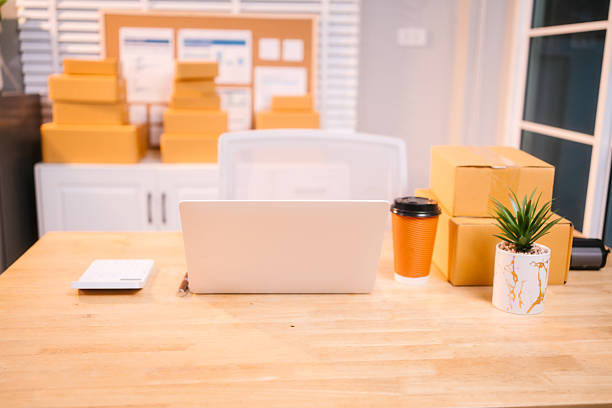 istock A neat workspace with a white laptop, stacked delivery boxes, a coffee cup, and a potted plant on a wooden desk, indicating a busy day of online sales packaging and fulfillment. 2217312557