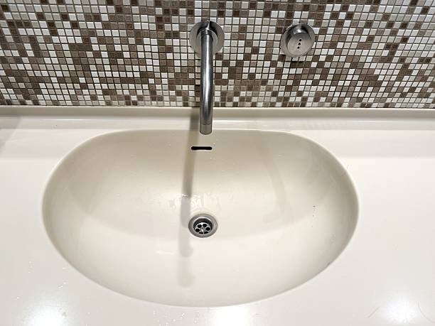 Contemporary bathroom interior showcasing a stylish white sink mounted against a rich brown mosaic tile wall. The warm earth tones of the tiles contrast beautifully with the clean lines of the modern sink, creating a balanced and elegant design. Ideal for themes related to interior design, home improvement, luxury living, and bathroom decor inspiration.