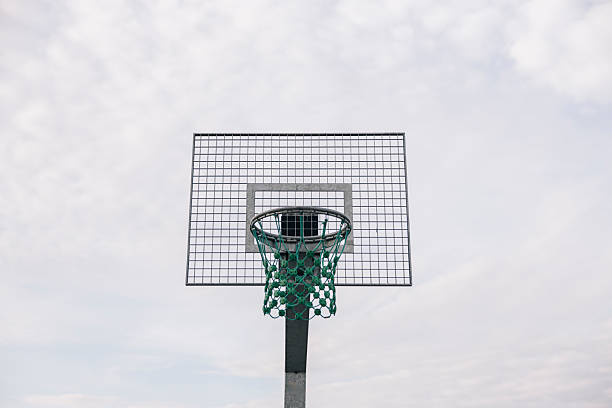 Basketball hoop with a green net against a cloudy sky, ready for a game
