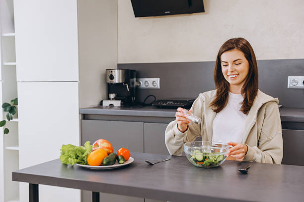 istock Young woman adding salt to her salad in modern kitchen 2217321340