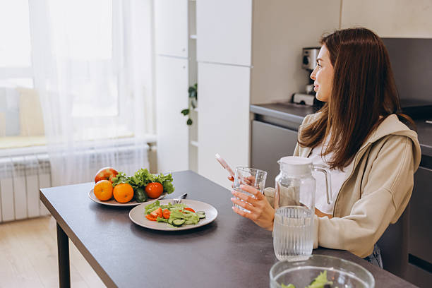 istock Young Woman Enjoying Healthy Meal and Browsing Smartphone in Modern Kitchen 2217321649