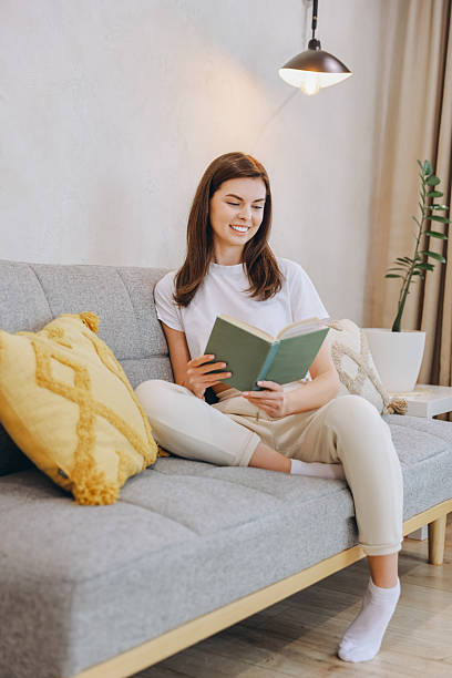 istock Young woman enjoying reading a book while relaxing on a comfortable sofa at home 2217321674