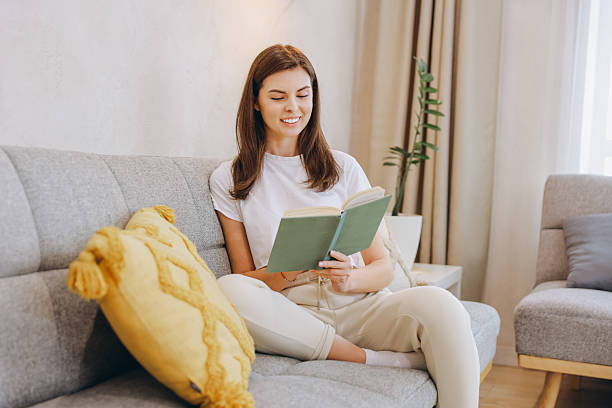 istock Smiling Woman Reading a Book While Relaxing on Comfortable Sofa at Home 2217321677