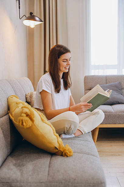 istock Young Woman Reading a Book While Relaxing on Sofa at Home 2217321907