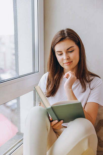 istock Young woman enjoying reading a book by the window 2217322110