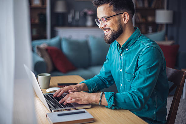 Young businessman working from home typing on laptop and smiling
