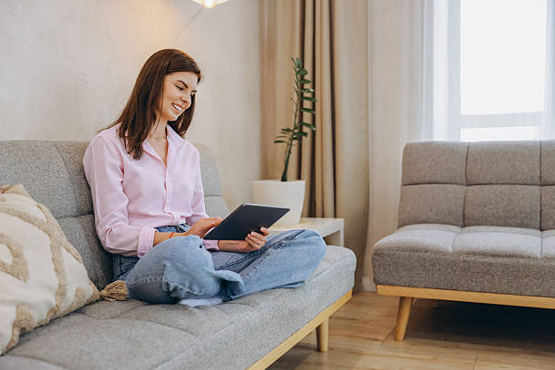istock Smiling Woman Using Tablet Sitting on Sofa at Home 2217324333