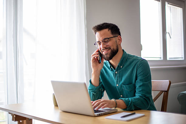 istock Young businessman working from home, using laptop and talking on the phone 2217324472